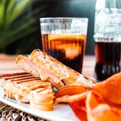 Sándwich mixto con queso fundido acompañado de chips y refresco en un restaurante Delicioso sándwich de jamón y queso derretido, ideal para menús de restaurante.