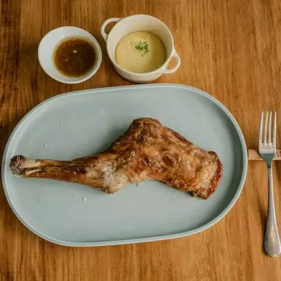 Pierna de cordero asada con guarniciones en mesa de madera. Del horno a tu mesa: pierna de cordero asada con puré cremoso y salsa al gusto.
